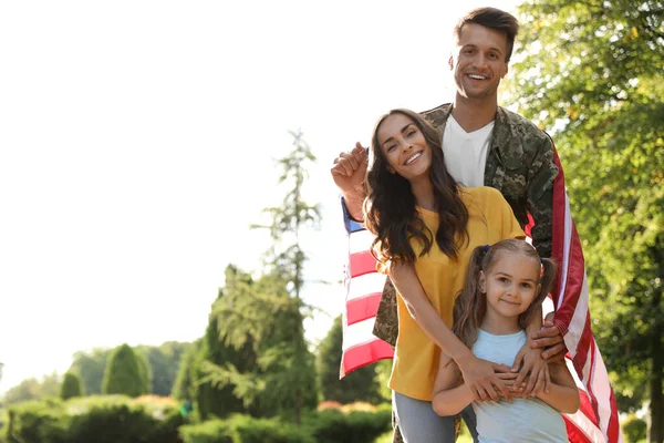 Homem de uniforme militar com bandeira americana e sua família no parque ensolarado — Fotografia de Stock