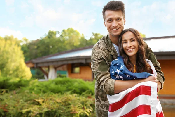 Homem de uniforme militar com bandeira americana e sua esposa ao ar livre — Fotografia de Stock