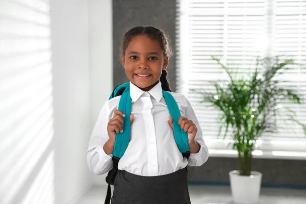 Glückliches afrikanisch-amerikanisches Mädchen in Schuluniform mit Rucksack drinnen — Stockfoto