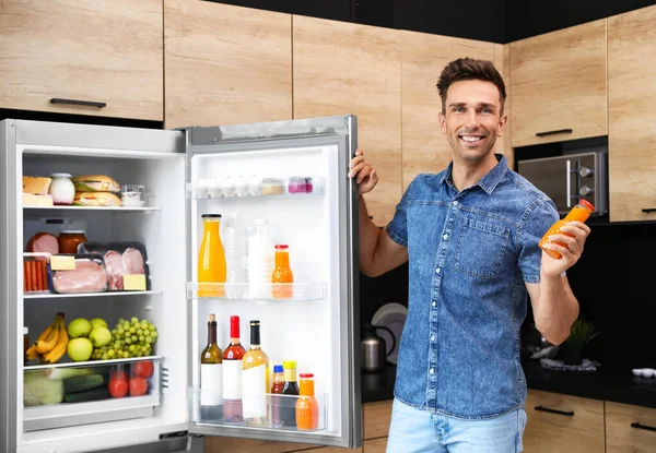 Hombre con botella de jugo cerca del refrigerador en la cocina — Foto de Stock