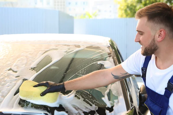 Молодой рабочий чистит автомобиль с губкой на автомойке — стоковое фото