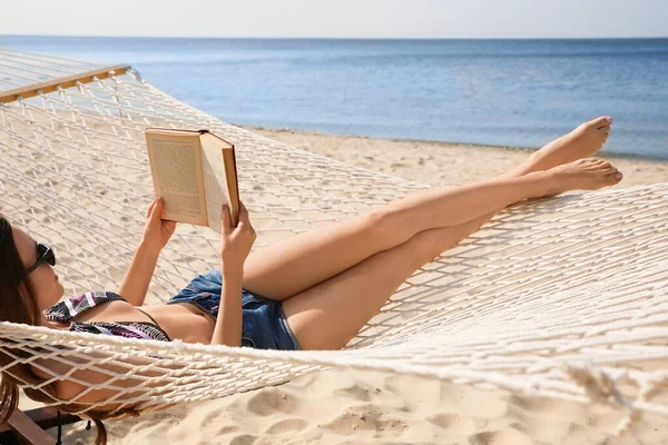 Jovem mulher lendo livro em rede na praia — Fotografia de Stock