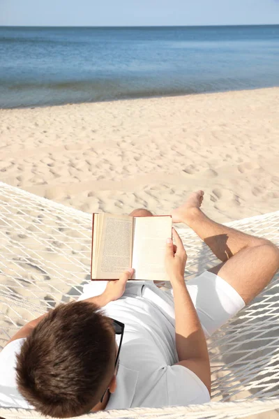 年轻人在海滩的吊床上看书 — 图库照片