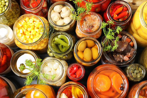 Open jars with pickled vegetables and dill inflorescences on grey table, flat lay
