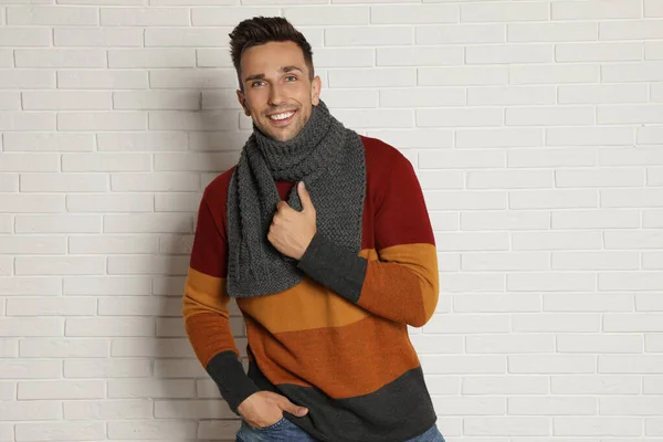 Happy young man in scarf and warm sweater near white brick wall. Winter season — Stock Photo, Image