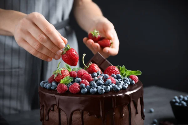 Kvinna dekorera läcker chokladkaka med färska jordgubbar vid bordet, närbild — Stockfoto