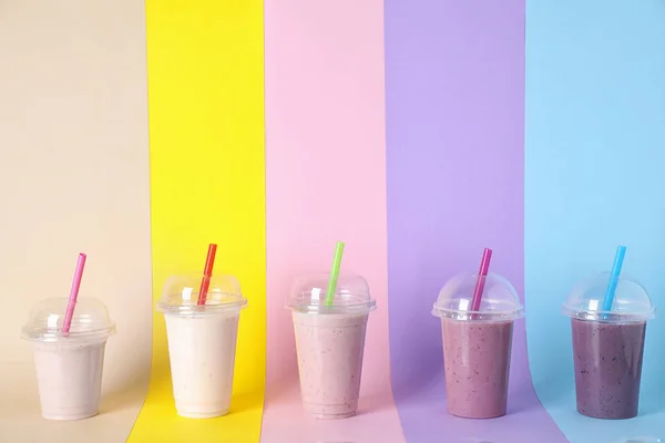 Διαφορετικές γευστικές μιλκσέικ σε πλαστικά ποτήρια στο φόντο χρώμα. Χώρος για κείμενο — Φωτογραφία Αρχείου