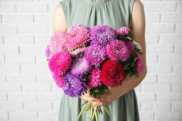 Kvinna innehav bukett med vackra aster blommor mot vit tegelvägg, närbild — Stockfoto