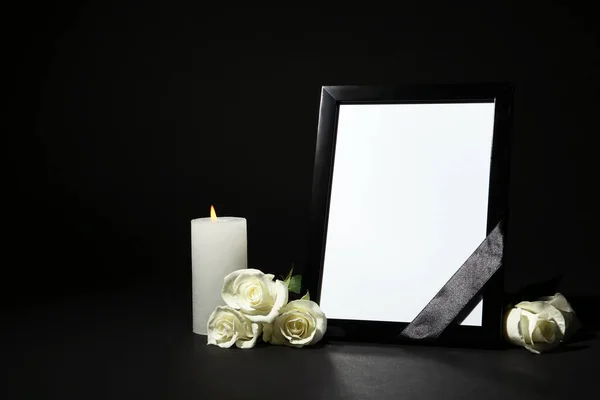 Marco fotográfico funerario con cinta, rosas blancas y vela sobre mesa oscura sobre fondo negro. Espacio para el diseño — Foto de Stock