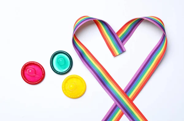 Preservativos coloridos y cinta de arco iris sobre fondo blanco, vista superior. Concepto LGBT — Foto de Stock