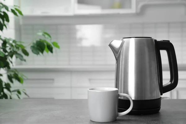 Modern electric kettle and cup on grey table in kitchen. Space for text — Stock Photo, Image