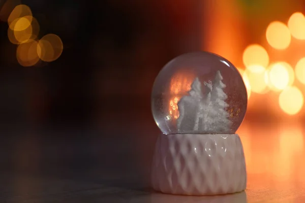 Globo de neve na mesa de madeira contra fundo desfocado, espaço para texto. Efeito Bokeh — Fotografia de Stock