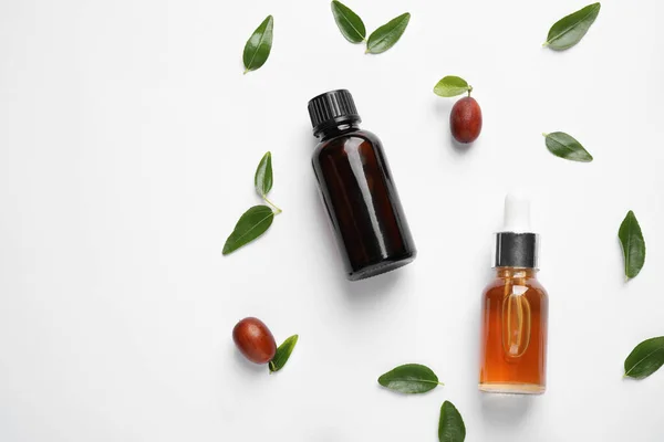 Glass bottles with jojoba oil and seeds on white background, top view