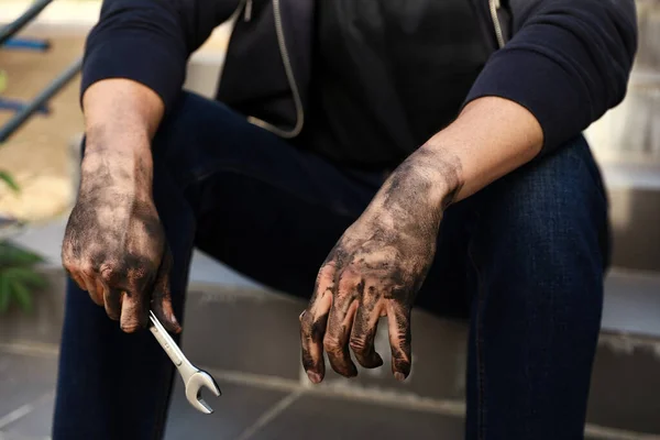 Dirty worker holding wrench on stairs, closeup of hands — Stock Photo, Image