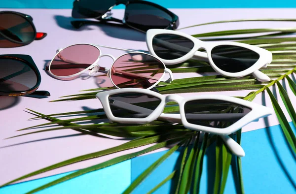 Стильні сонцезахисні окуляри та тропічний лист на кольоровому фоні. час відпустки — стокове фото
