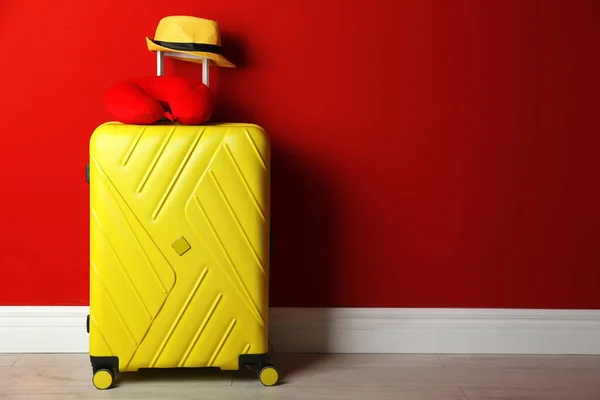 Жовта валіза, капелюх і подушка для подорожей біля червоної стіни, простір для тексту — стокове фото