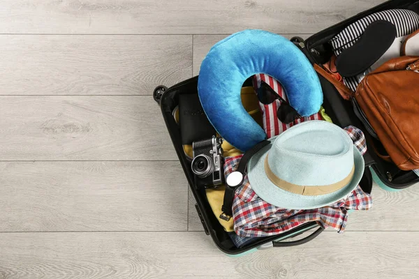 Otwarta walizka z poduszką podróżną i ubraniami na drewnianej podłodze, widok z góry. Miejsce na tekst — Zdjęcie stockowe