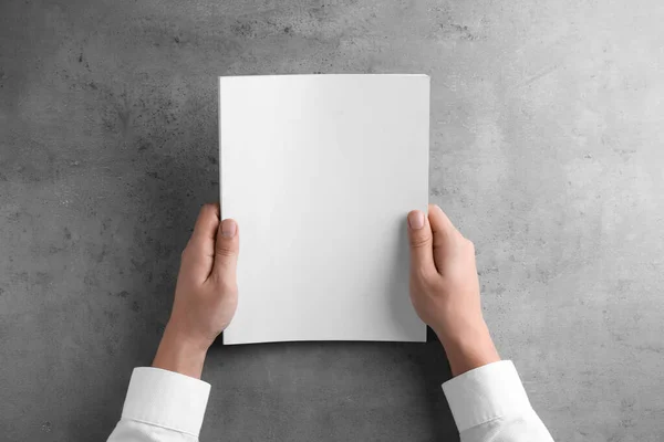 Homem segurando livreto em branco na mesa cinza, vista superior. Mock up para o projeto — Fotografia de Stock