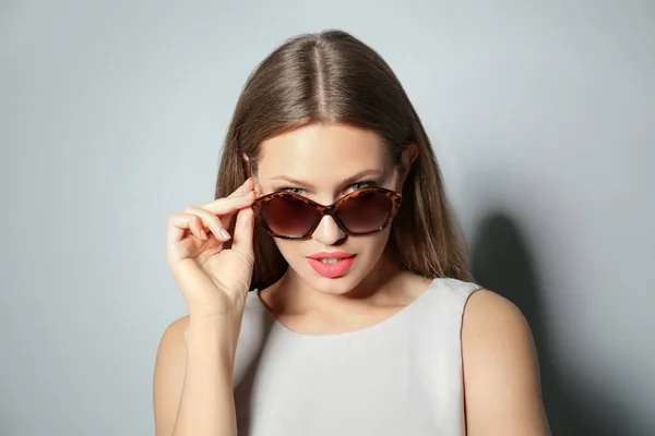 Mujer joven con gafas de sol elegantes sobre fondo gris claro — Foto de Stock