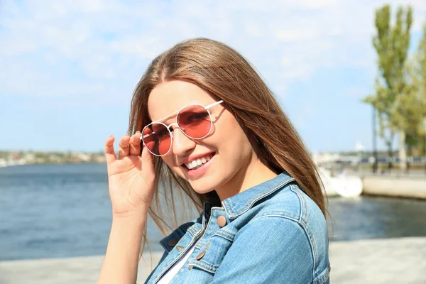 Młoda kobieta w stylowych okularach przeciwsłonecznych w pobliżu rzeki — Zdjęcie stockowe