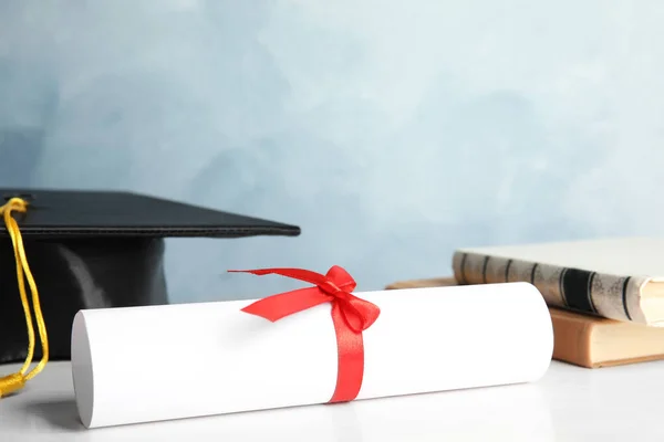 Δίπλωμα αποφοίτησης μαθητή σε λευκό ξύλινο τραπέζι με φόντο γαλάζιο — Φωτογραφία Αρχείου