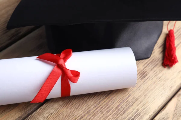 Sombrero de graduación y diploma de estudiante en mesa de madera, primer plano — Foto de Stock