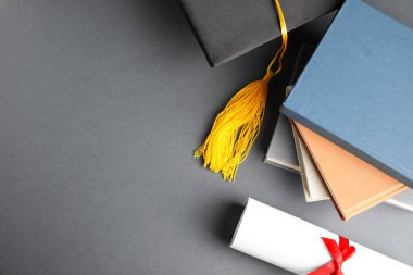 Mezuniyet şapkası ve gri arkaplan üzerine öğrenci diploması ile düz kompozisyon, metin için boşluk