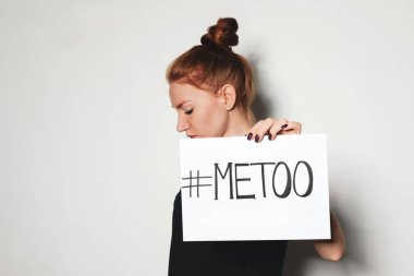 Young woman holding #METOO card against light background clipart