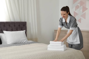 Oda hizmetçisi otel odasında yatağa temiz havlu koyuyor. Metin için alan