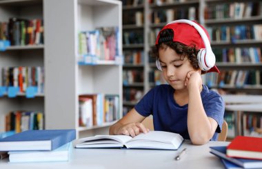 Kütüphanede kitap okuyan kulaklıklı şirin bir çocuk.