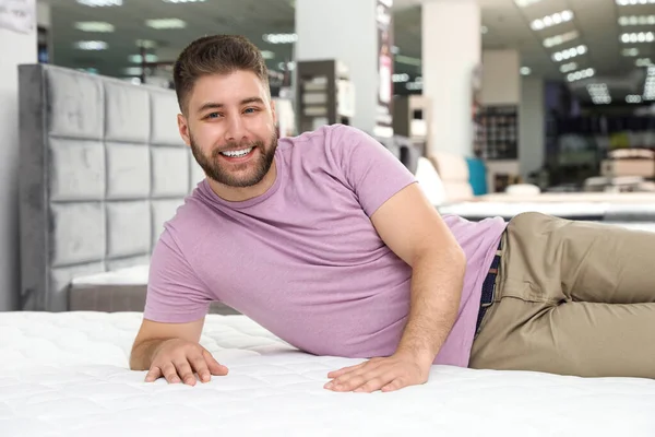 Улыбающийся мужчина лежит на ортопедическом матрасе в магазине — стоковое фото