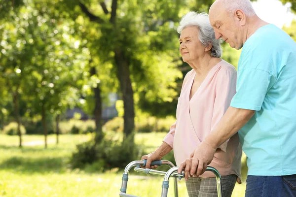 Homem idoso ajudando sua esposa com andar quadro ao ar livre — Fotografia de Stock