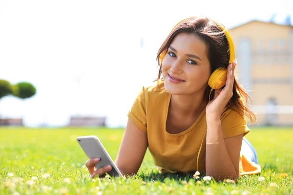 Νεαρή γυναίκα με ακουστικά που ακούει μουσική στο πάρκο. Χώρος για κείμενο — Φωτογραφία Αρχείου