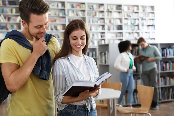 Jovens felizes com livro na biblioteca — Fotografia de Stock