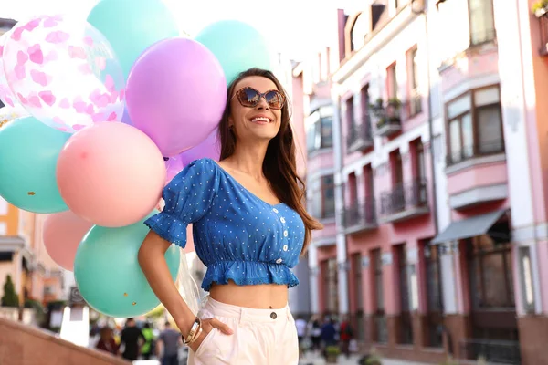 Piękna młoda kobieta z kolorowymi balonami na ulicy miasta — Zdjęcie stockowe