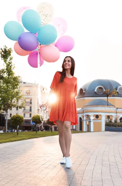 Wesoła młoda kobieta z kolorowymi balonami na świeżym powietrzu w słoneczny dzień — Zdjęcie stockowe