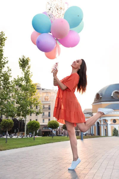 Fröhliche junge Frau mit bunten Luftballons an sonnigen Tagen im Freien — Stockfoto