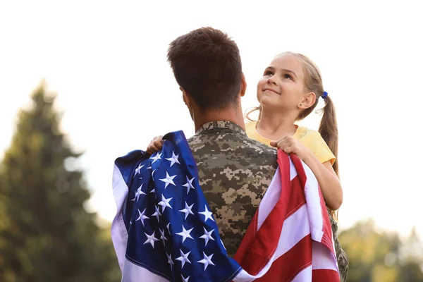 Apa katonai egyenruhában, amerikai zászlóval és lányával a napos parkban. — Stock Fotó