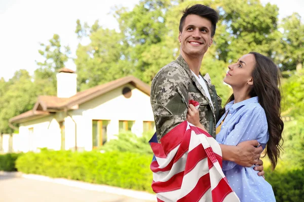 Homem de uniforme militar com bandeira americana abraçando sua esposa ao ar livre — Fotografia de Stock