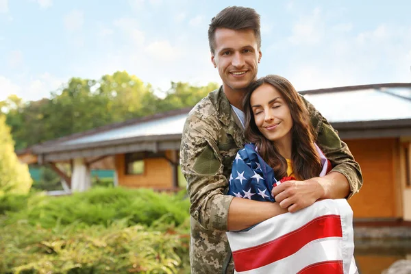 Hombre en uniforme militar con bandera americana y su esposa al aire libre — Foto de Stock