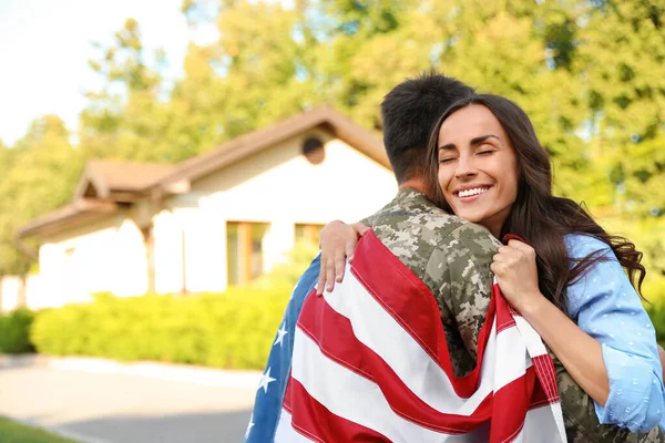 Homem de uniforme militar com bandeira americana abraçando sua esposa ao ar livre — Fotografia de Stock
