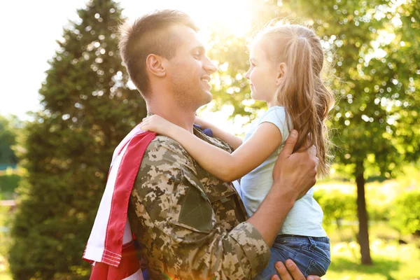 Pai de uniforme militar com bandeira americana segurando sua filhinha no parque verde — Fotografia de Stock