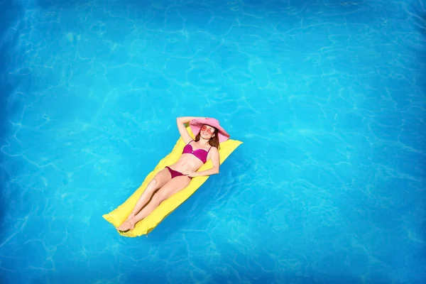 Young woman on inflatable mattress in swimming pool, above view