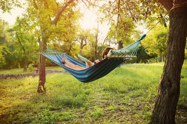 Young woman reading book in comfortable hammock at green garden — Stock Photo, Image