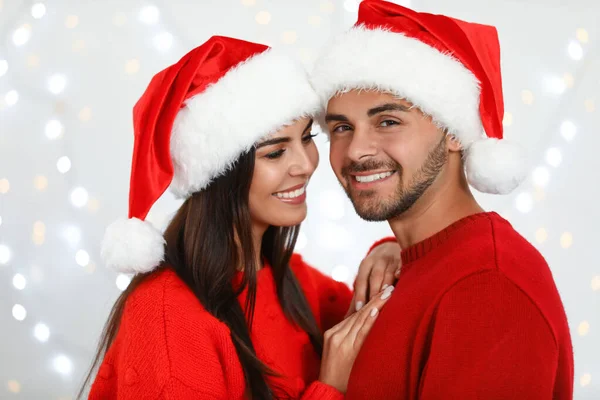 Preciosa pareja joven en los sombreros de Santa contra las luces borrosas festivas. Celebración de Navidad —  Fotos de Stock