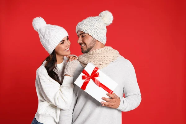 Härligt ungt par med presentask på röd bakgrund. Julfirande — Stockfoto