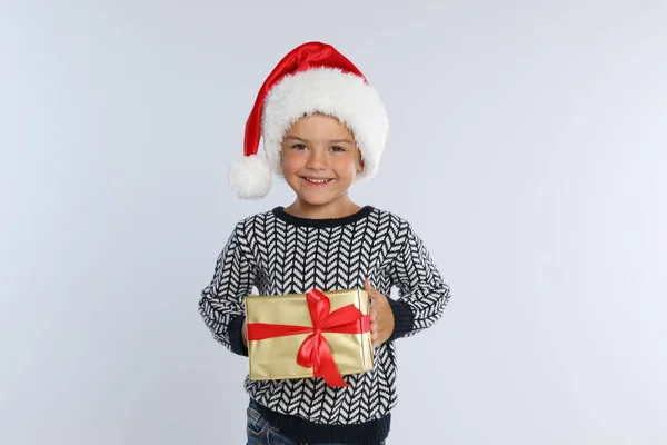 Щаслива маленька дитина в Санта-Каті з подарунковою коробкою на світло-сірому фоні. Свято Різдва — стокове фото