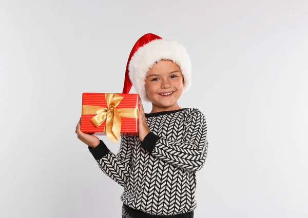 Criança feliz em chapéu de Papai Noel com caixa de presente em fundo cinza claro. Celebração de Natal — Fotografia de Stock