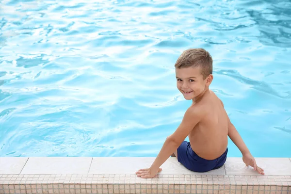 Bonito menino sentado perto da piscina exterior — Fotografia de Stock