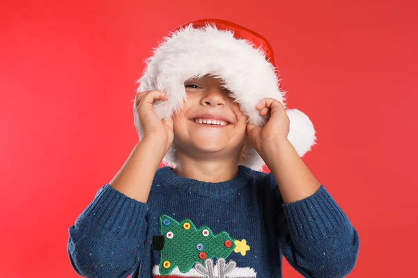 Счастливый маленький ребенок в шляпе Санты на красном фоне. Праздник Рождества — стоковое фото